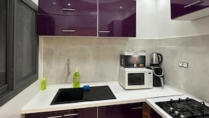 A modern kitchen with dark purple cabinets, a white countertop, a black sink, a stove, and a microwave. - DAKAR VDN: Furnished apartment for rent- 2 bedrooms- Living room - 3 bathrooms (Dakar)