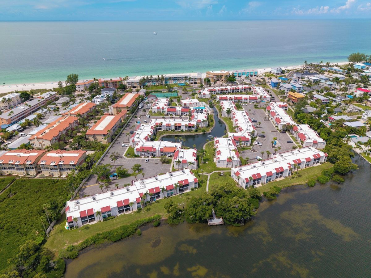 Ein Luftbild eines Küstenresorts mit mehreren Gebäuden, einer Marina und einem Strand.