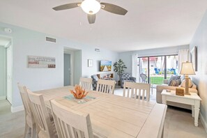 A dining area with a wooden table and chairs, a ceiling fan, and a view of the backyard through a glass door. - The Holiday House at Runaway Bay 159 (Bradenton Beach)