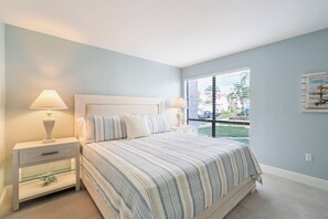 A bedroom with a bed, nightstands, and a window with blinds. - The Holiday House at Runaway Bay 159 (Bradenton Beach)