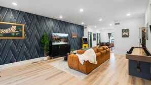 A modern living room with a large TV, a sofa, a pool table, and a dining area. - Modern Group Oasis: Hot Tub, Arcade & Fire Pit (St. Louis)