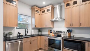 A modern kitchen with wooden cabinets, stainless steel appliances, and a window with blinds. - Modern Group Oasis: Hot Tub, Arcade & Fire Pit (St. Louis)