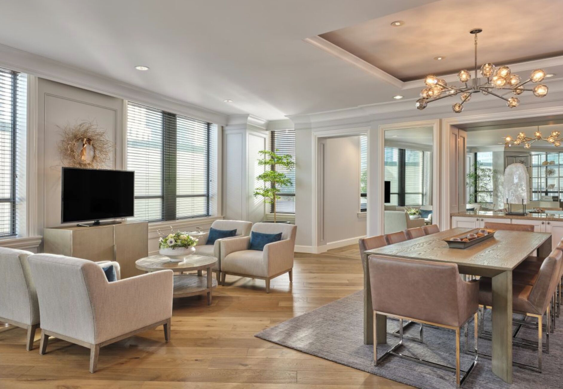 A spacious living room with a flat-screen TV, comfortable seating, a dining area with a table, and large windows.