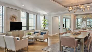 A spacious living room with a flat-screen TV, comfortable seating, a dining area with a table, and large windows.