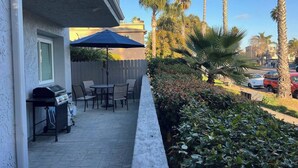 Une terrasse extérieure avec un barbecue, des chaises et une table, le tout installé sous un parasol bleu.