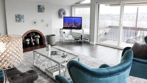 En moderne stue med et fladskærms-tv, en pejs og en balkon med udsigt over byen.