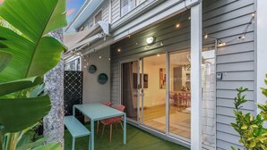 Une maison moderne dotée d’un patio couvert, d’une porte-fenêtre coulissante donnant sur un espace de salle à manger intérieur, et d’un petit coin salon extérieur avec une table et des chaises.
