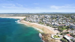 Vista aerea di una città costiera con spiaggia, edifici residenziali a grattacielo e uno stadio.