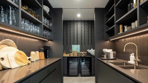 Uma cozinha moderna com armários escuros, uma ilha central com pia e prateleiras com copos e utensílios de cozinha.