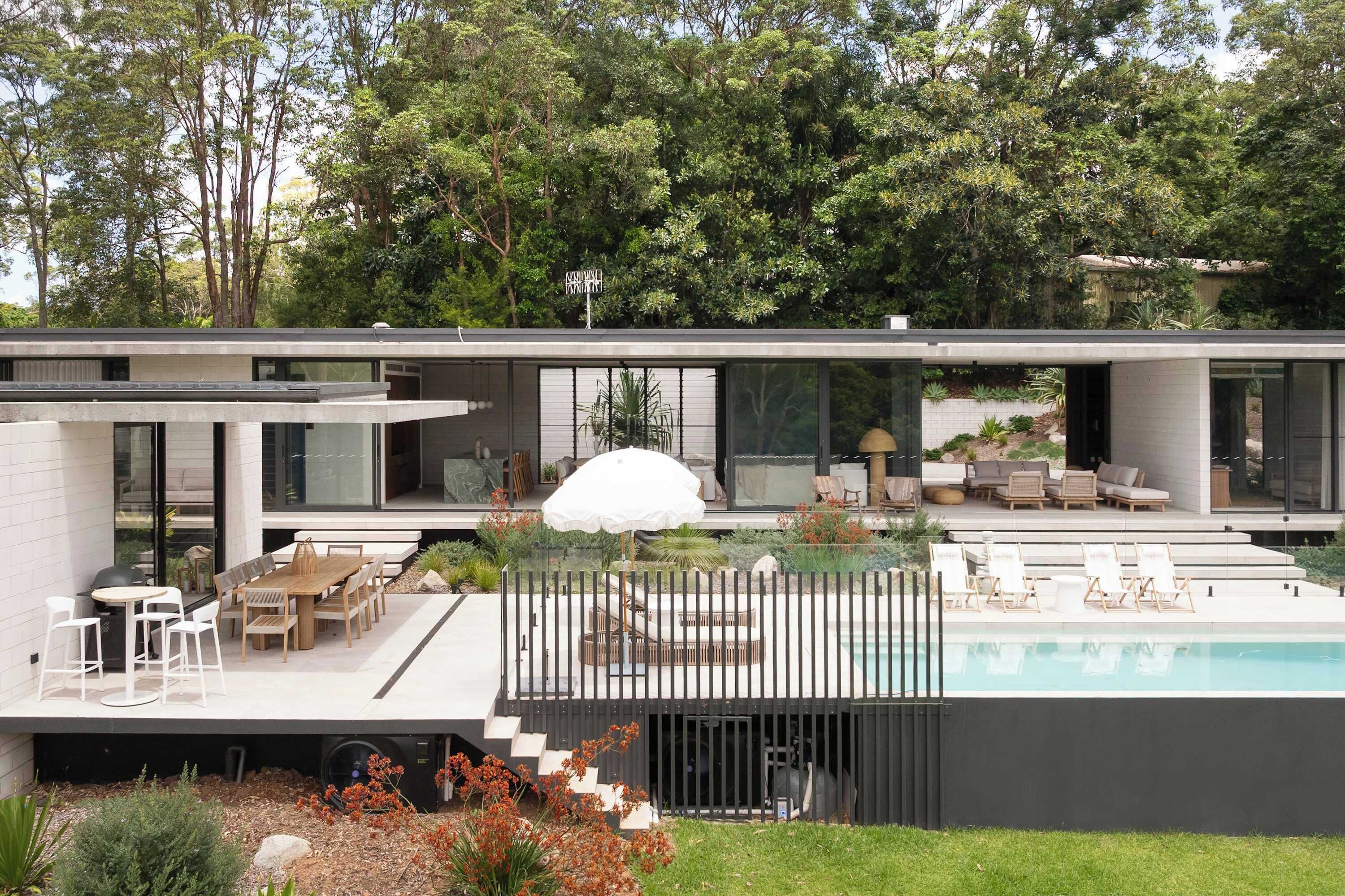 Une maison moderne dotée d’une piscine, d’un espace salon extérieur et d’un jardin.
