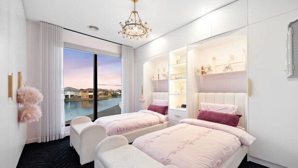A hotel room with two beds, a large window with a view of a pool and buildings, and built-in shelving with decorative items. - Elegant Waterfront Escape – Point Cook

Relax with the whole family. (Point Cook)