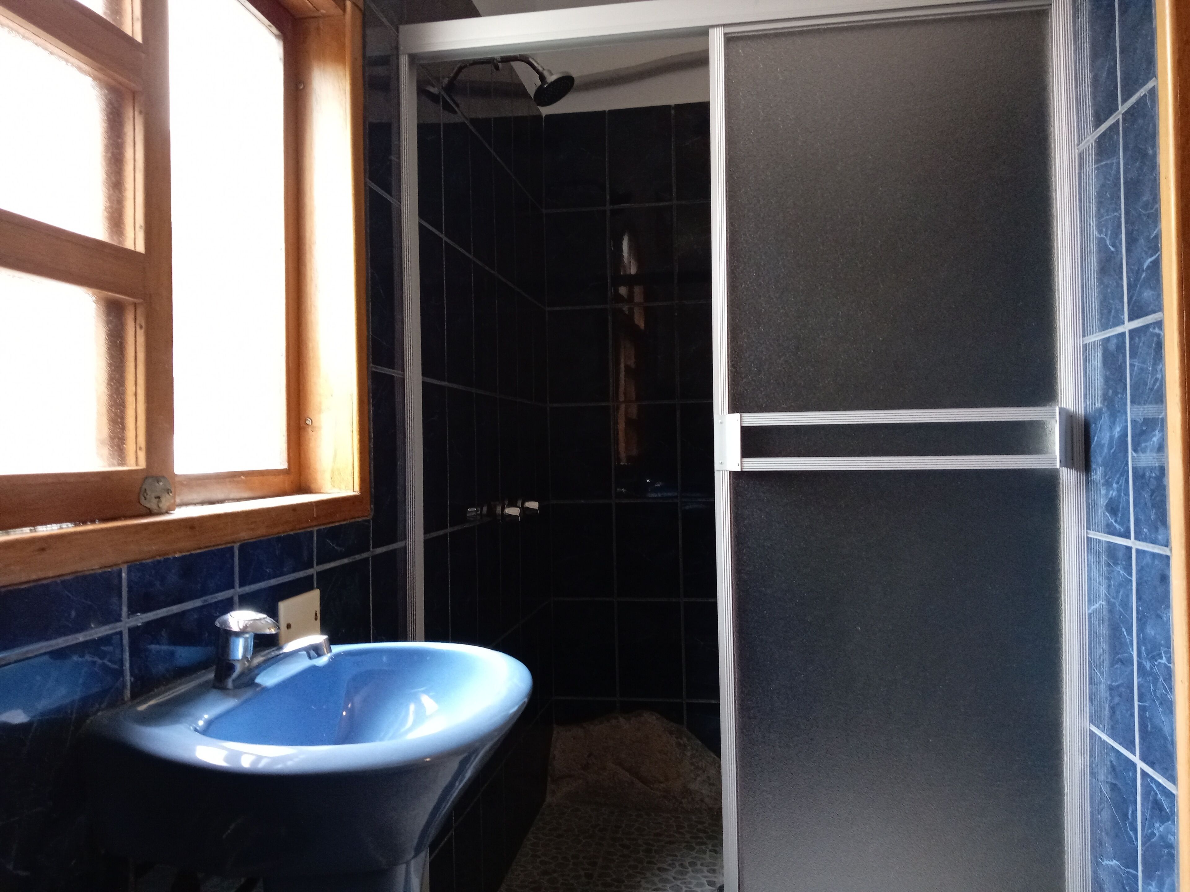 Un baño con un lavabo azul, ducha y azulejos azul oscuro.