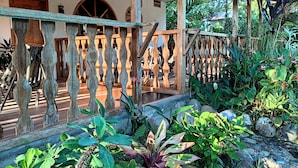 A covered outdoor area with a wooden railing, surrounded by lush tropical plants and a stone pathway. - Banana Lodge (Puerto Misahuallí)