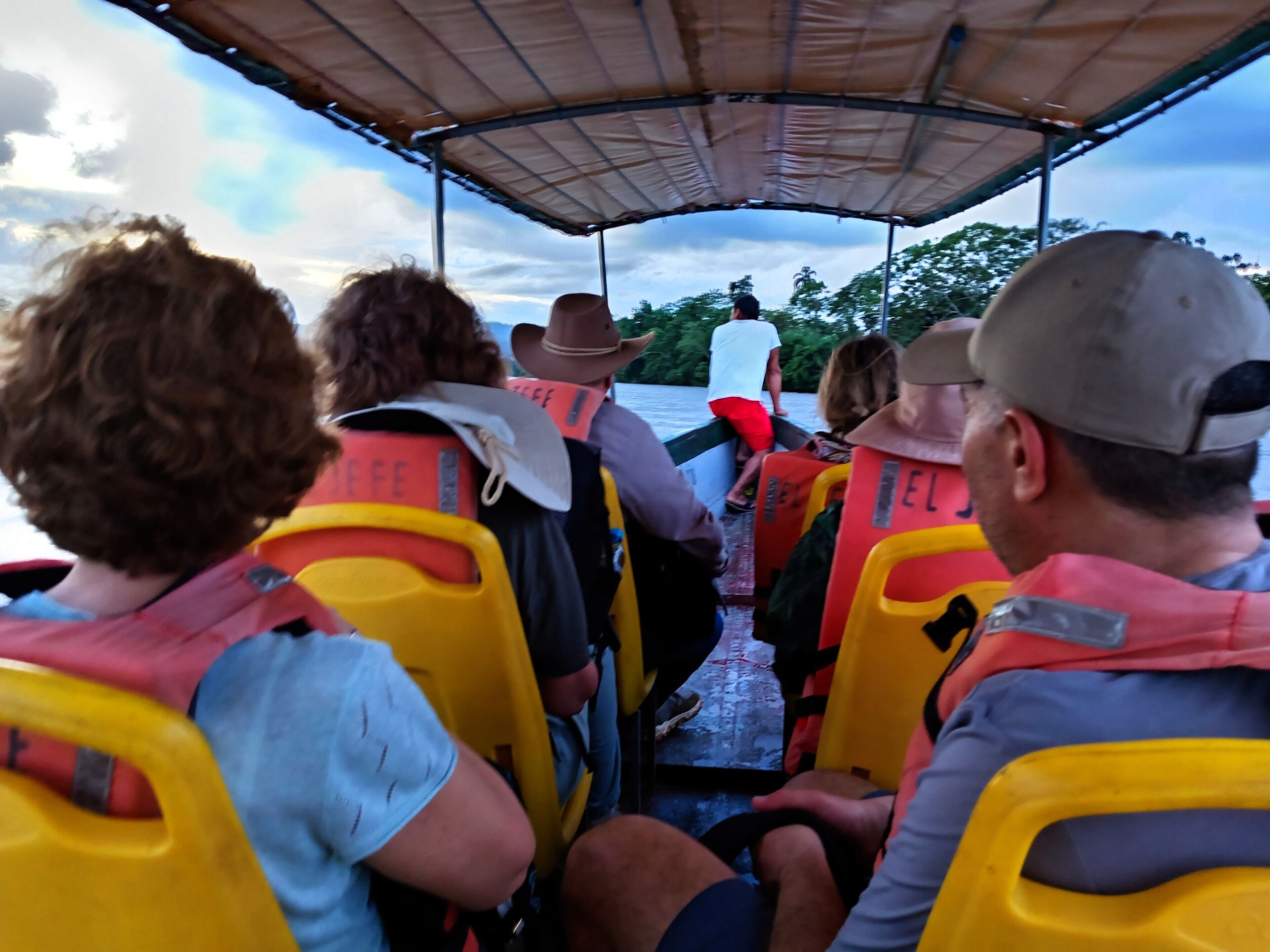 Un grupo de personas en un bote, con chalecos salvavidas y un toldo sobre sus cabezas.