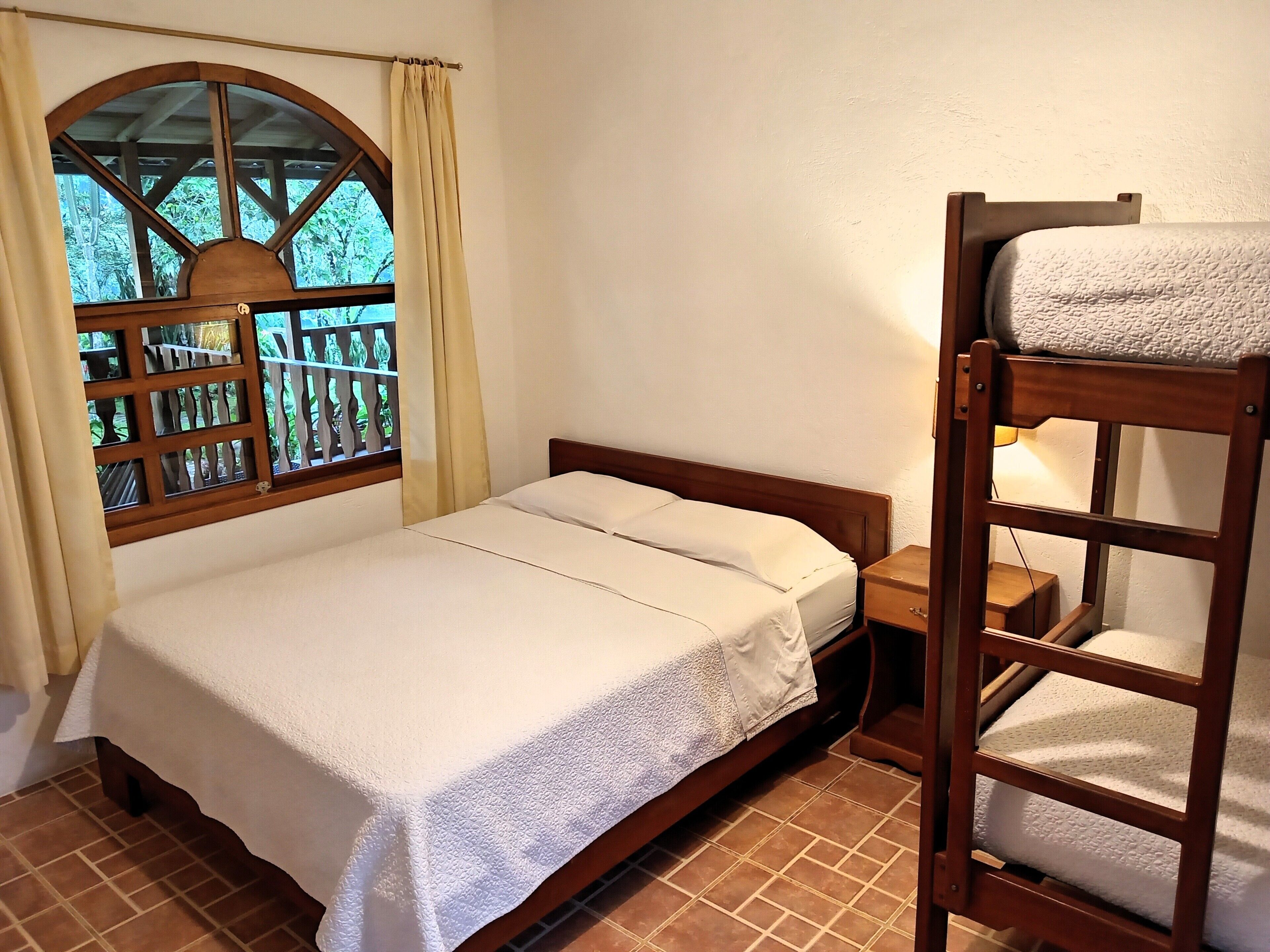 A single bed with a wooden headboard, a small bedside table, and a window with a view of greenery.