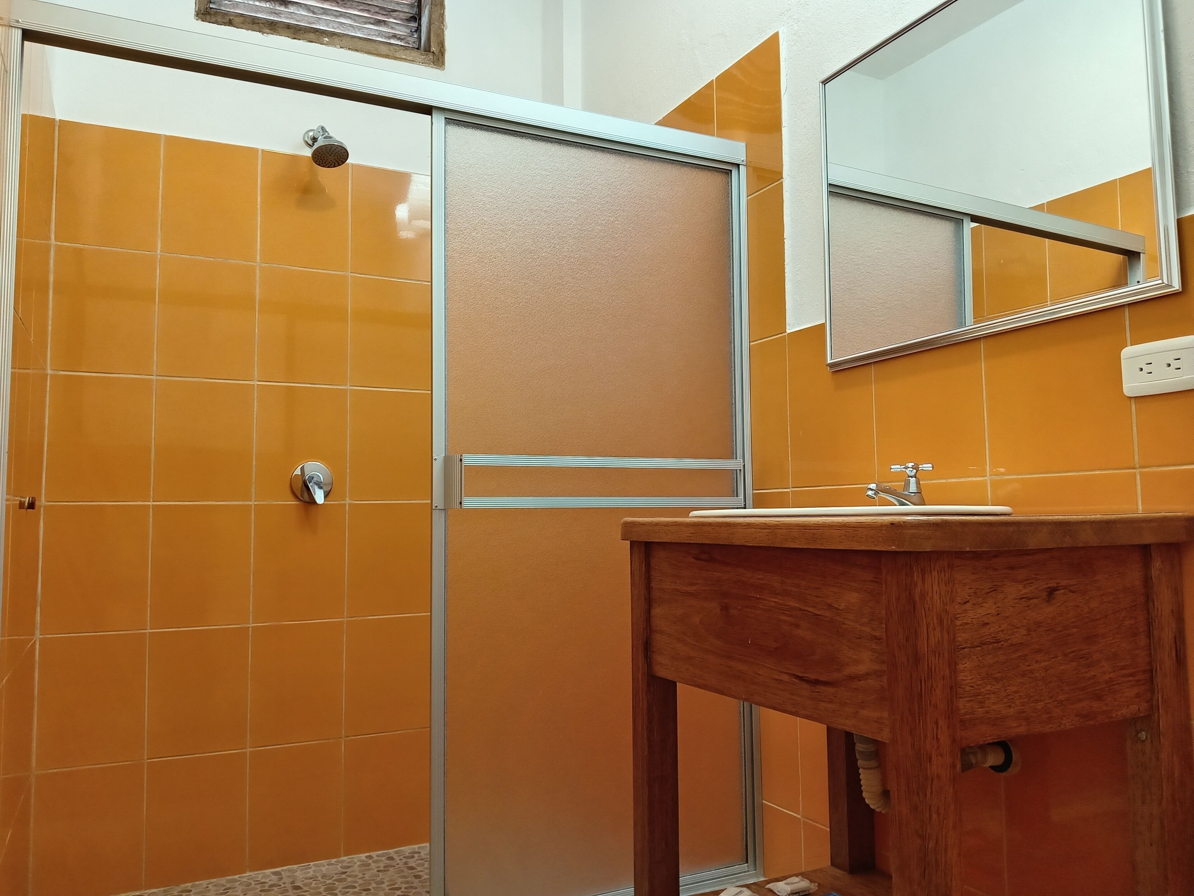 A bathroom with orange tiles, a glass shower enclosure, a wooden vanity, and a mirror.