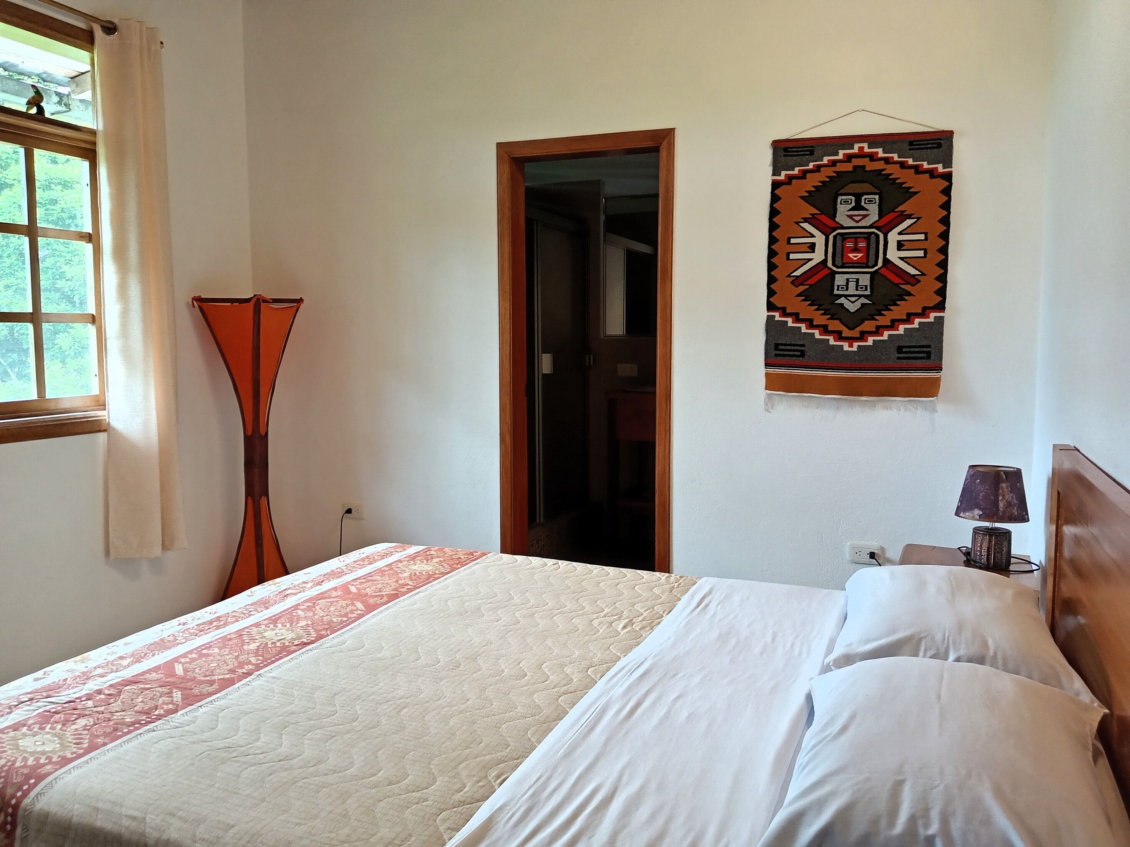 A bedroom with a bed, a hanging wall decoration, a lamp, and a window with curtains.