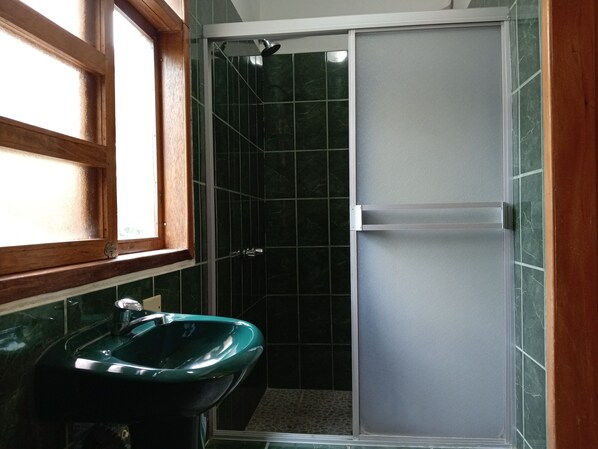 Une salle de bain avec un lavabo vert, une douche avec une porte coulissante et une fenêtre.