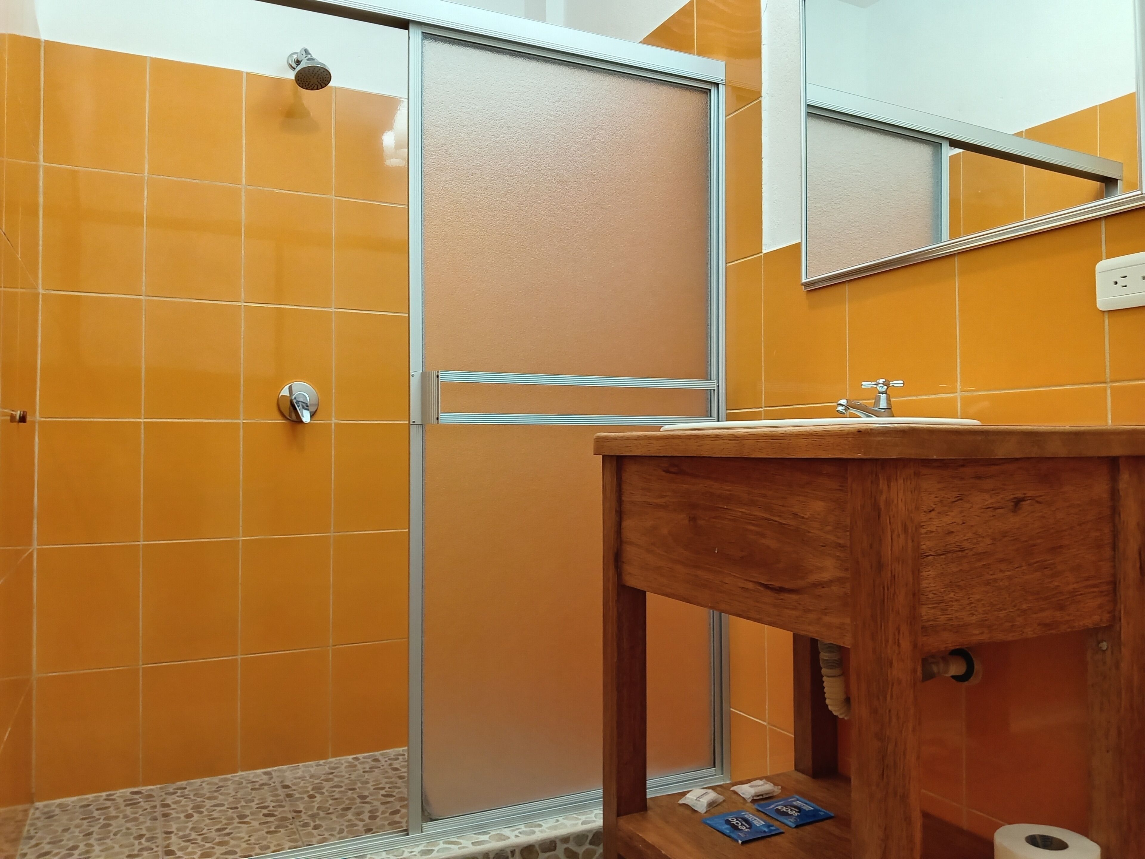 A bathroom with orange tiles, a wooden vanity, a glass shower enclosure, and a mirror.