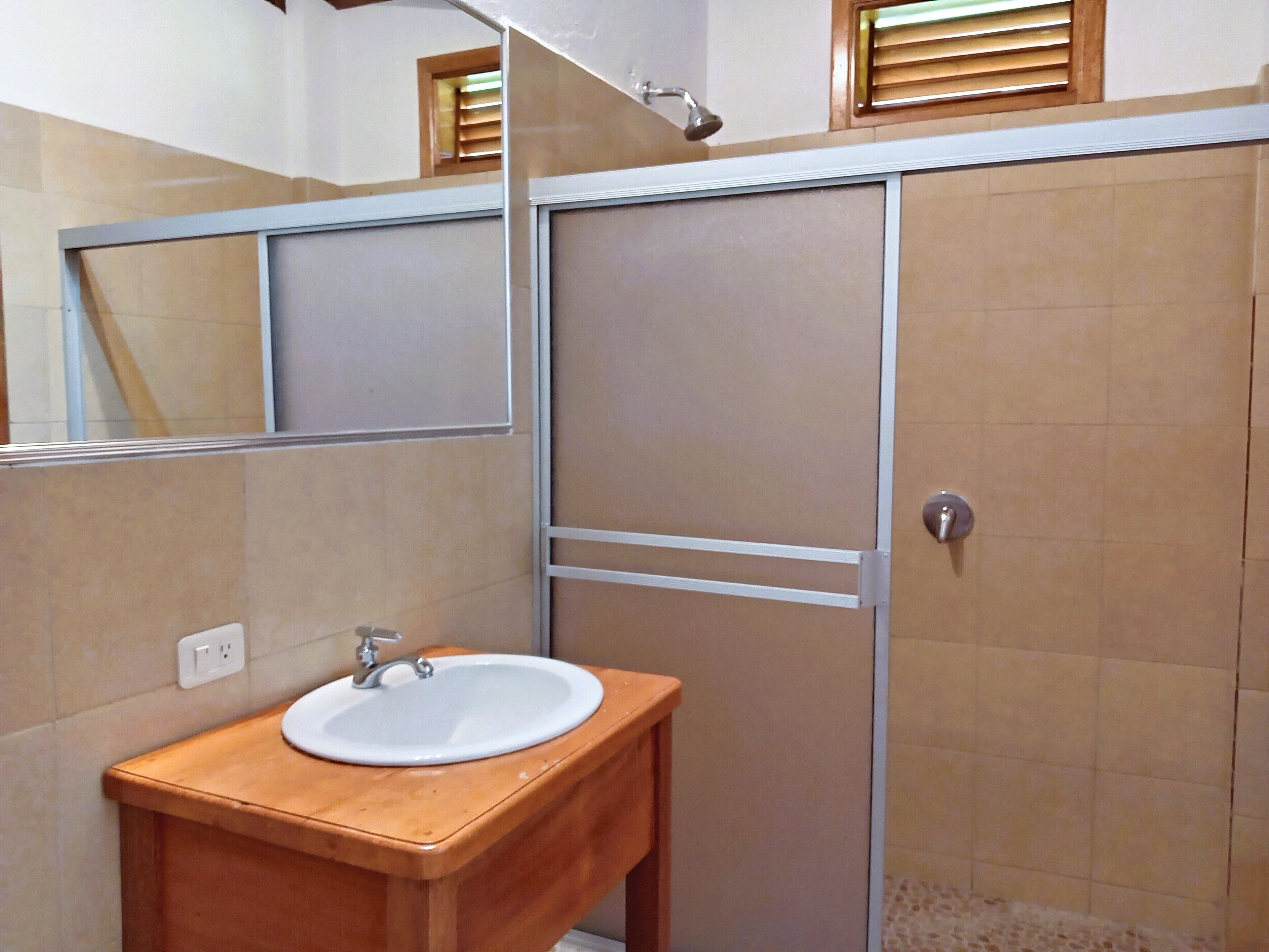 Un baño con tocador de madera, lavabo blanco y espejo.