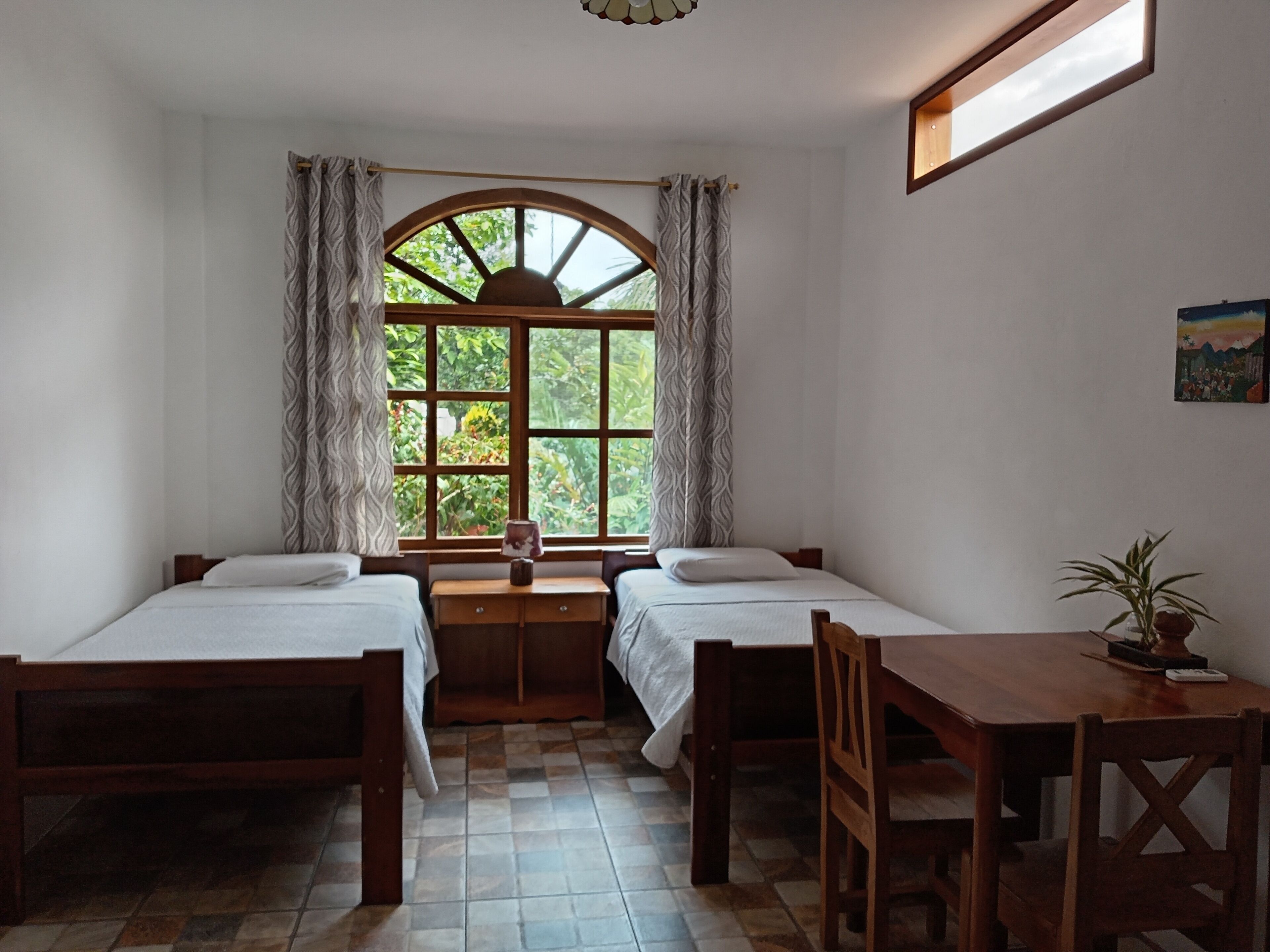 Een kamer met twee bedden, een houten tafel en een raam met gordijnen.