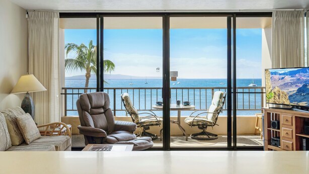 Une chambre d’hôtel dotée d’un grand balcon, d’un canapé, d’un fauteuil inclinable, d’une télévision et d’une armoire en bois.