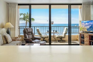 A hotel room with a large balcony, a sofa, a recliner, a TV, and a wooden cabinet. - Direct Oceanfront unit that will take your breath away. Sugar Beach 528 (Kihei)