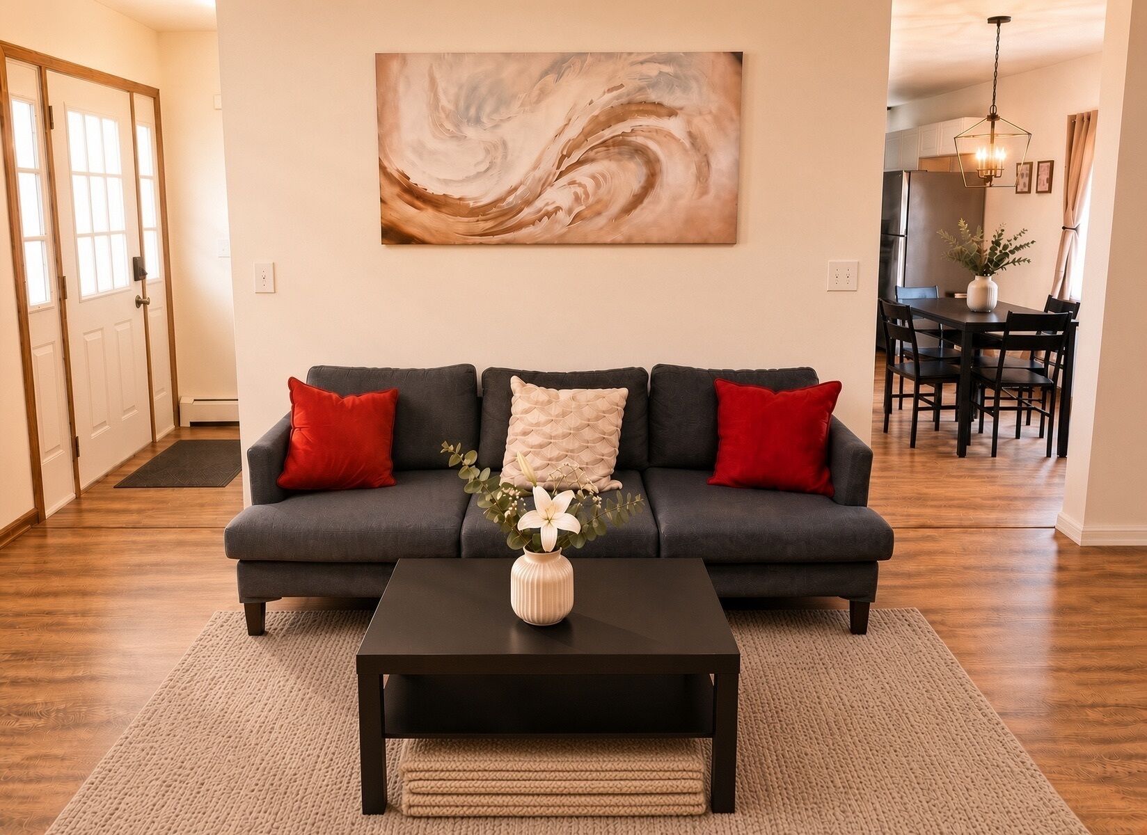 Una sala de estar con un sofá gris oscuro, cojines rojos y beige, una mesa de centro negra y un jarrón con flores.