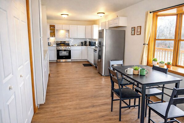 Een moderne keuken met witte kasten, roestvrijstalen apparatuur en een eethoek met een tafel en stoelen.