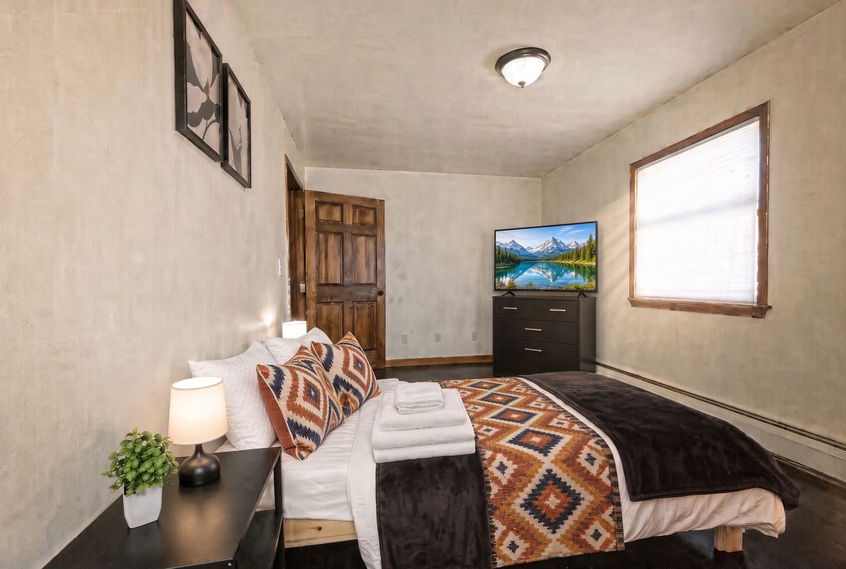 Een slaapkamer met een bed, een televisie, een raam en een deur.
