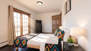 Une chambre d’hôtel avec un lit, une commode, une télévision, une porte et une fenêtre avec des rideaux.