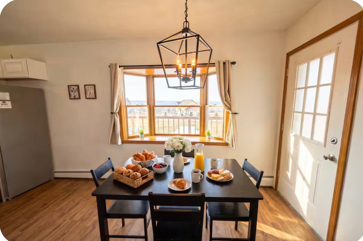 Un coin repas avec une table mise pour le petit-déjeuner, une fenêtre avec des rideaux et un luminaire suspendu.
