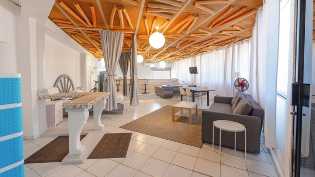 A spacious living area with a wooden ceiling, a dining table, a sofa, and a kitchen in the background. - Central Sosúa Studio: Pool, Fast Wi-Fi, Workspace (Sosúa)