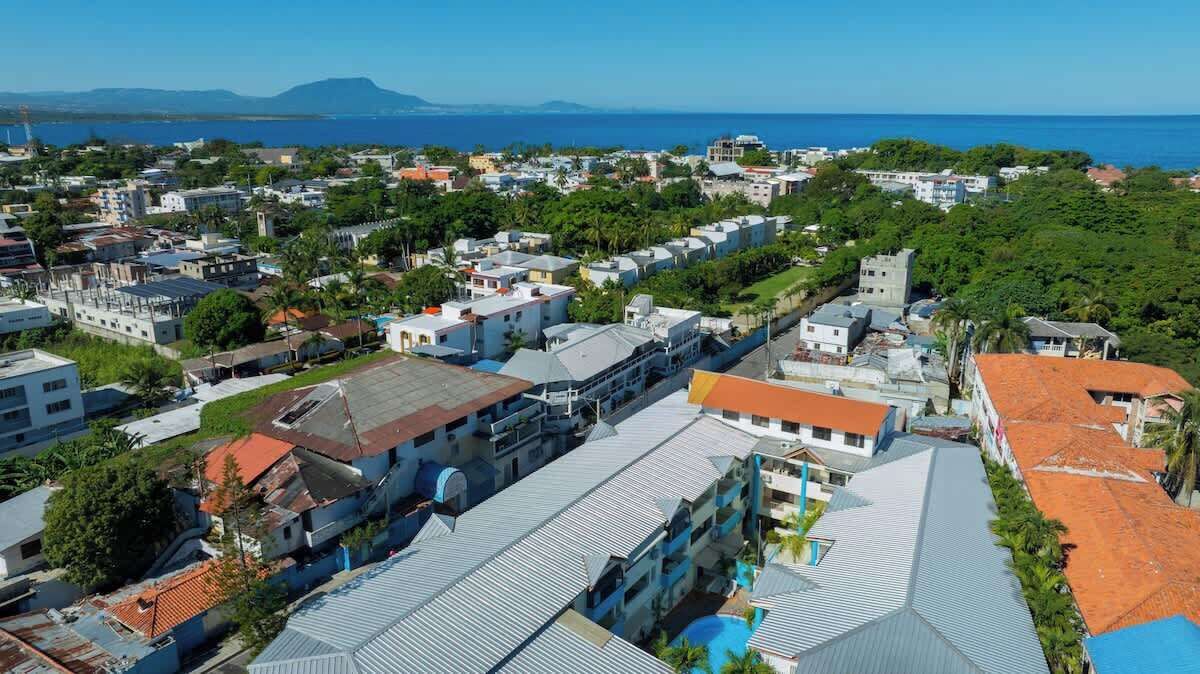 A coastal town with a mix of residential and commercial buildings, including a prominent hotel with a swimming pool and a view of the sea.