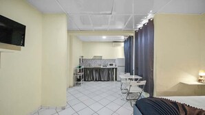 Une chambre d’hôtel avec un lit, un bureau, une chaise, un téléviseur et, au fond, une kitchenette.