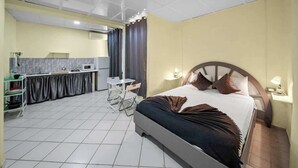 Une chambre d’hôtel avec un grand lit, un petit bureau, une chaise et un coin cuisine.