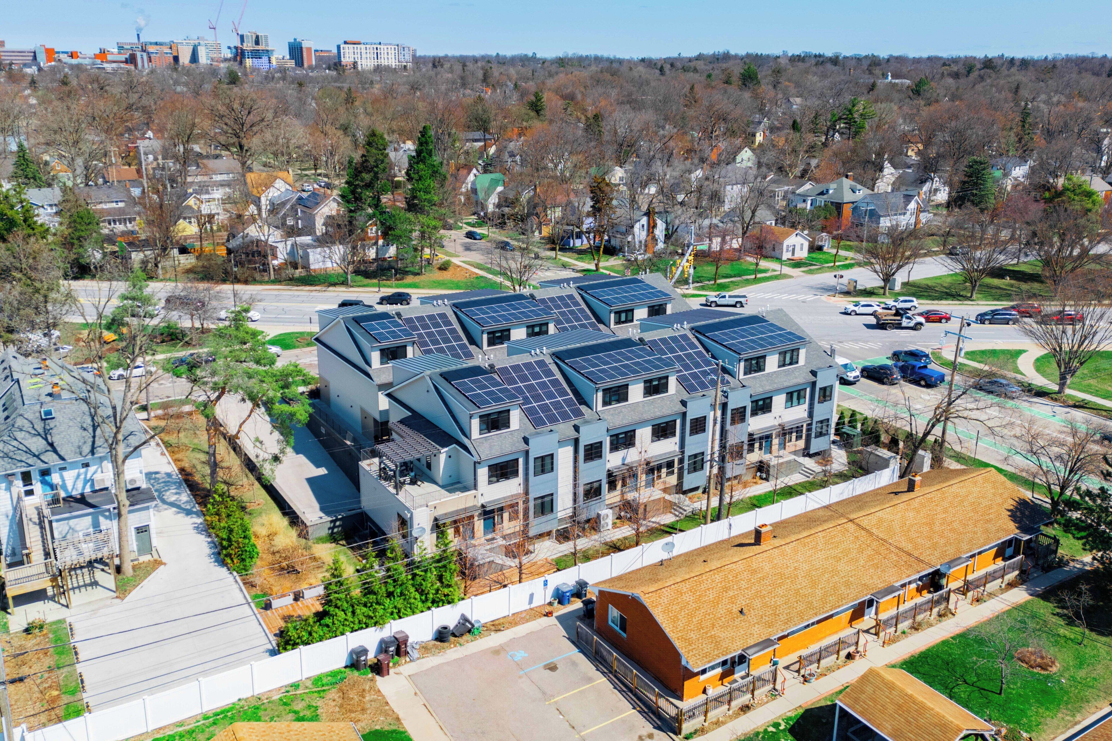 Un immeuble à plusieurs étages, doté de panneaux solaires sur le toit, situé dans un quartier résidentiel.