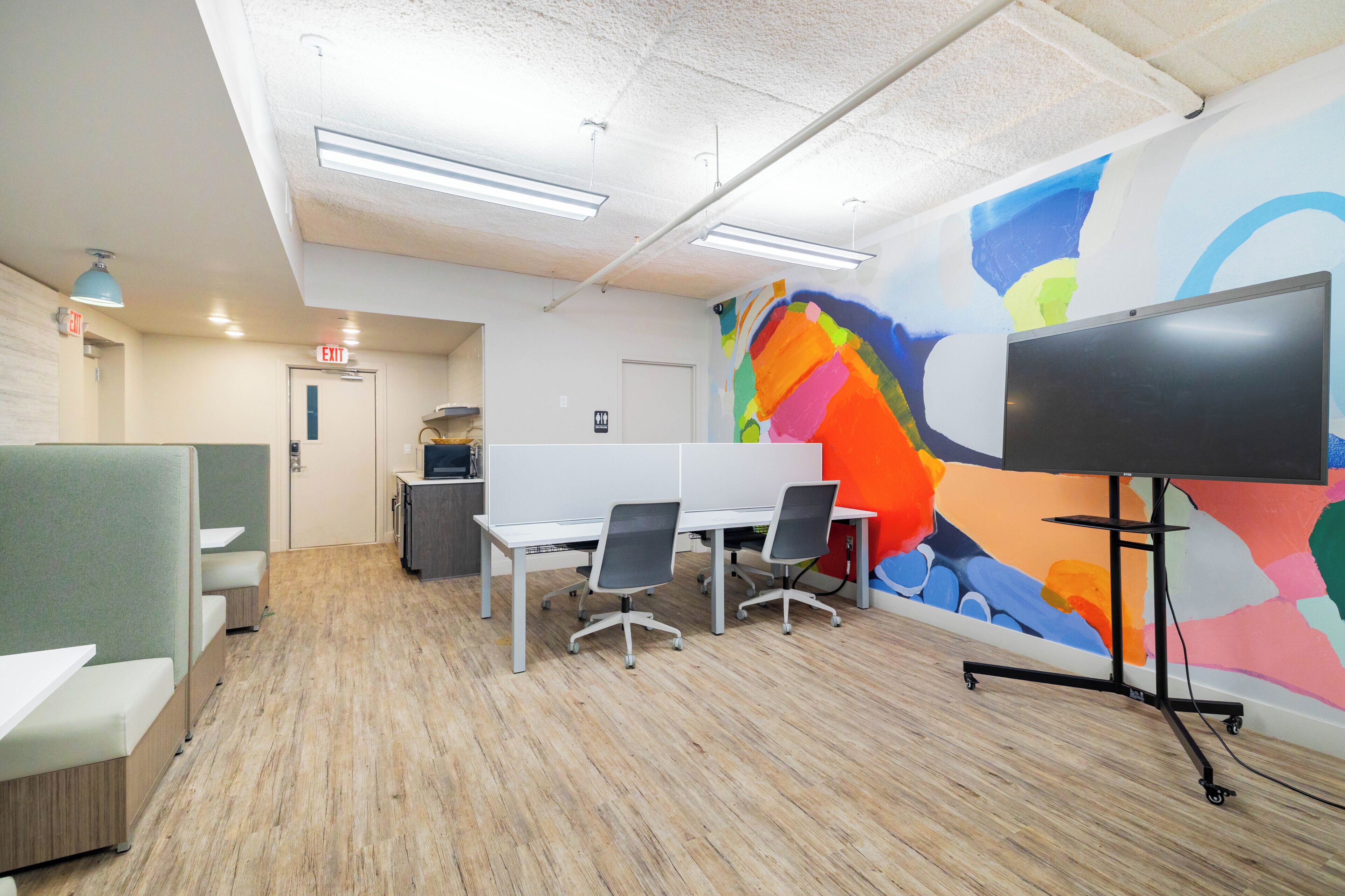A modern office space with cubicles, a large screen, and a colorful mural.