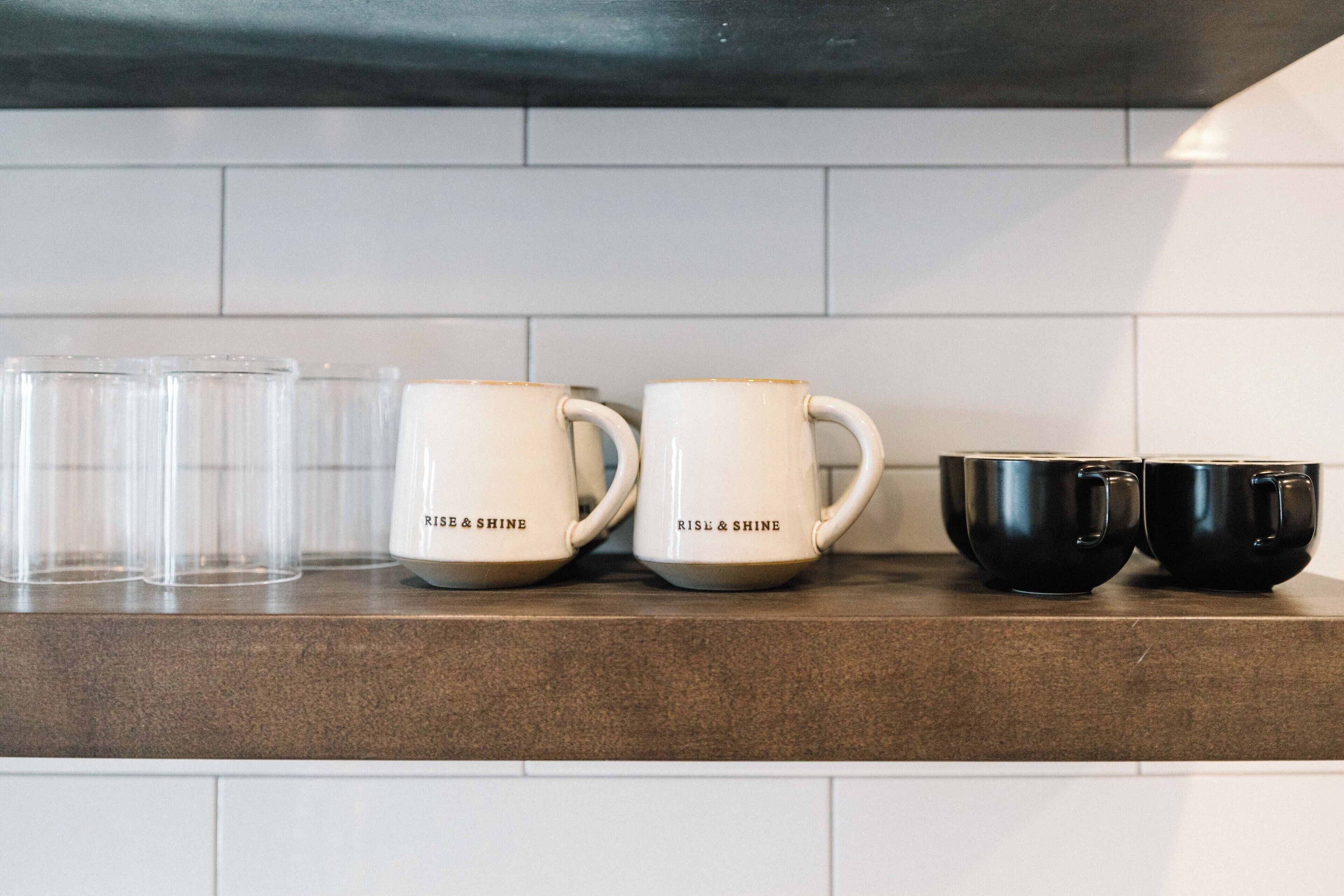 Eine Küchenarbeitsplatte mit vier Kaffeetassen, zwei davon mit der Aufschrift "RISE & SHINE" und zwei schlicht gehalten.