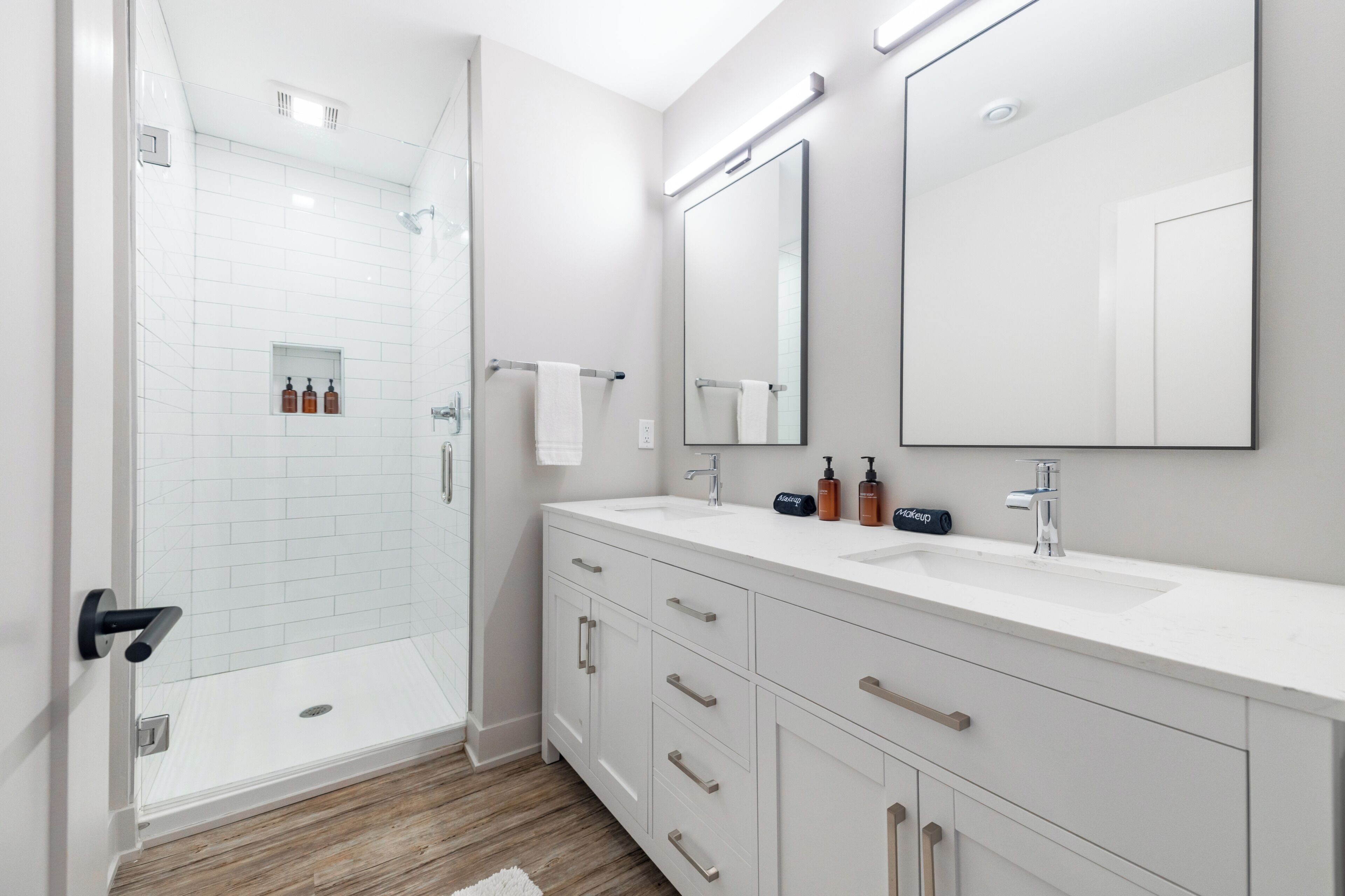 Un bagno moderno con cabina doccia in vetro, mobile lavabo bianco e un'ampia specchiera, oltre a una doccia a ingresso libero.