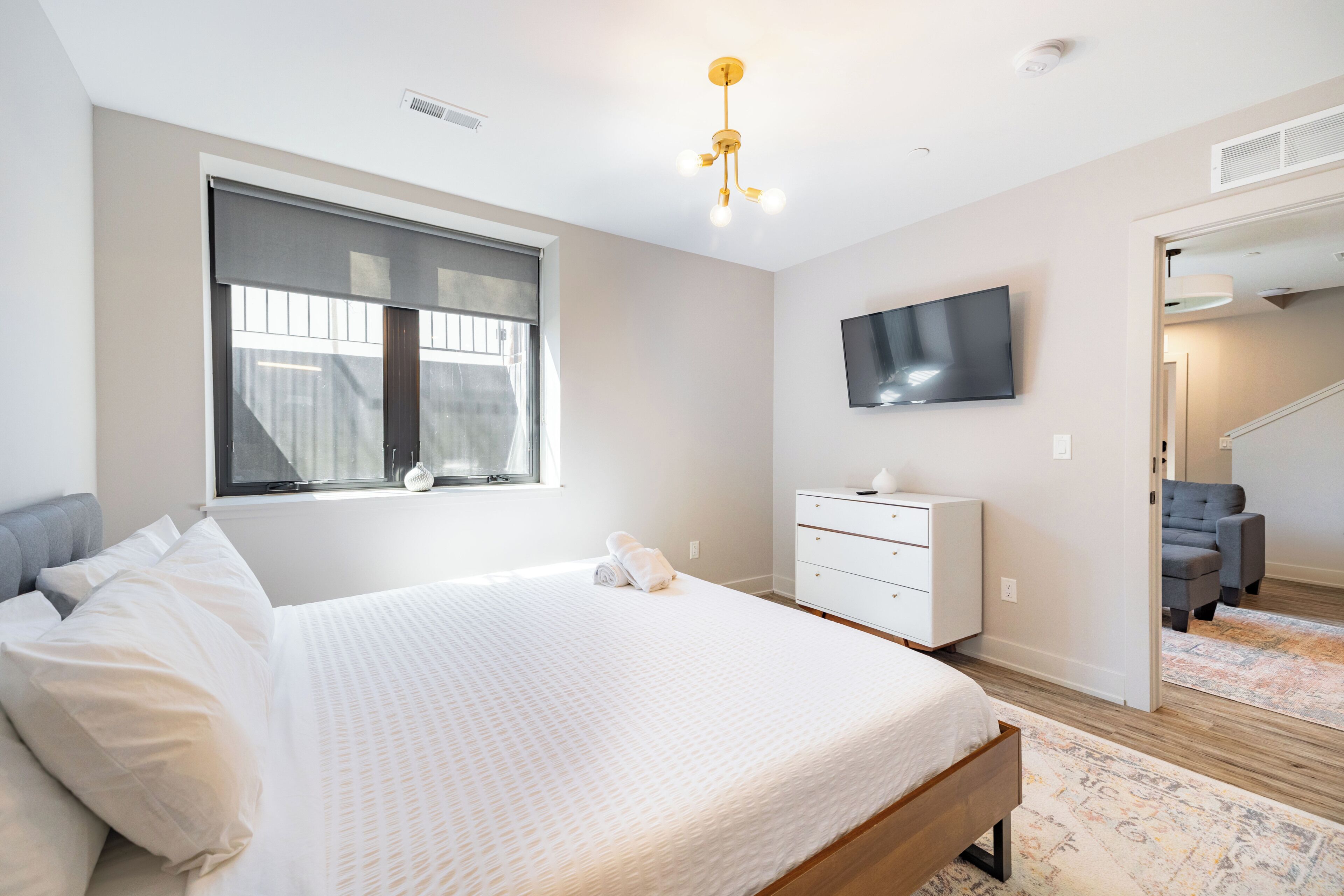Un dormitorio con una cama grande, un televisor en la pared, una ventana con persianas y una escalera que conduce a otra habitación.