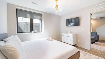 Un dormitorio con una cama grande, un televisor en la pared, una ventana con persianas y una escalera que conduce a otra habitación.