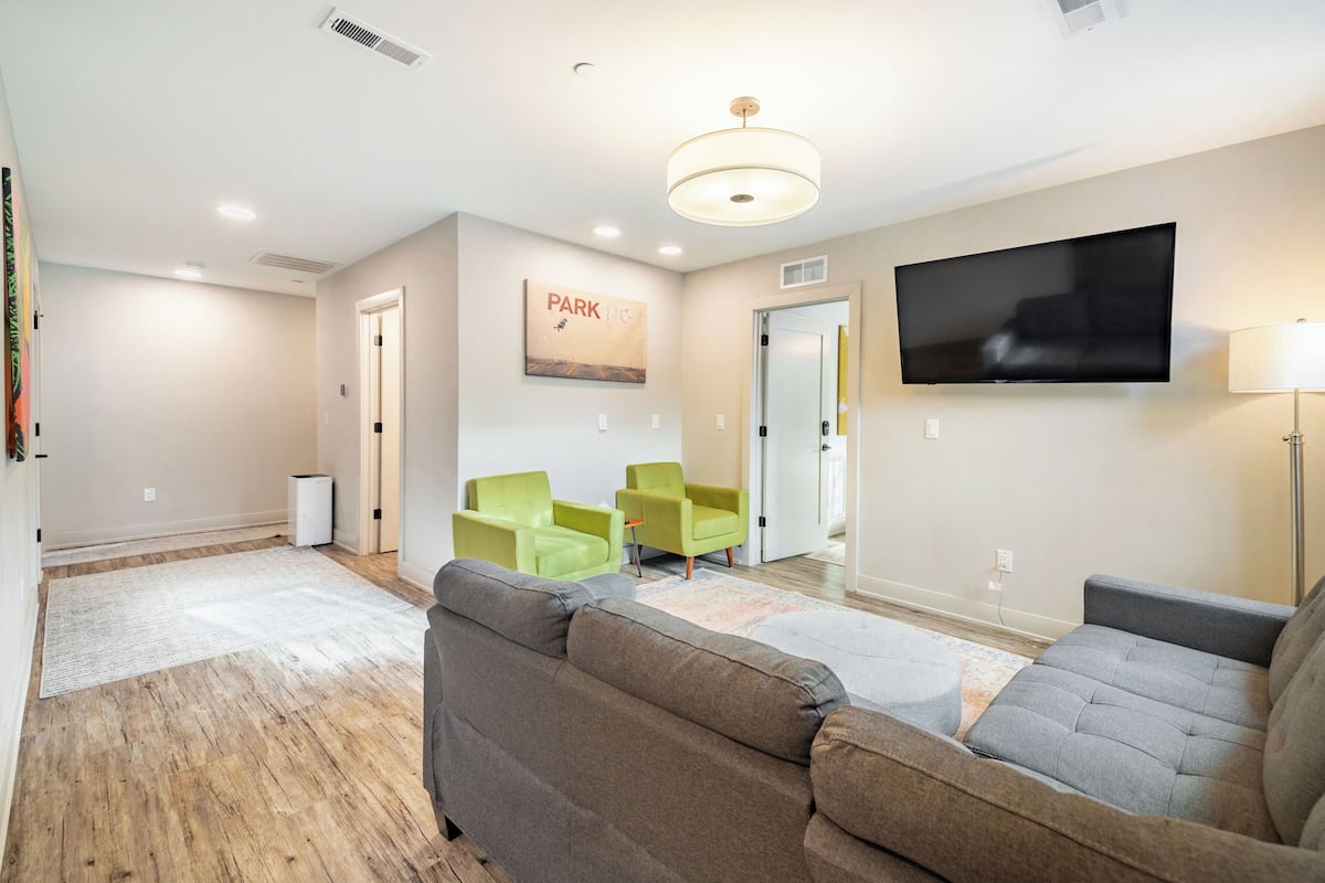 A modern living room with a grey sofa, green chairs, a flat-screen TV, and a 'PARKING' sign on the wall.