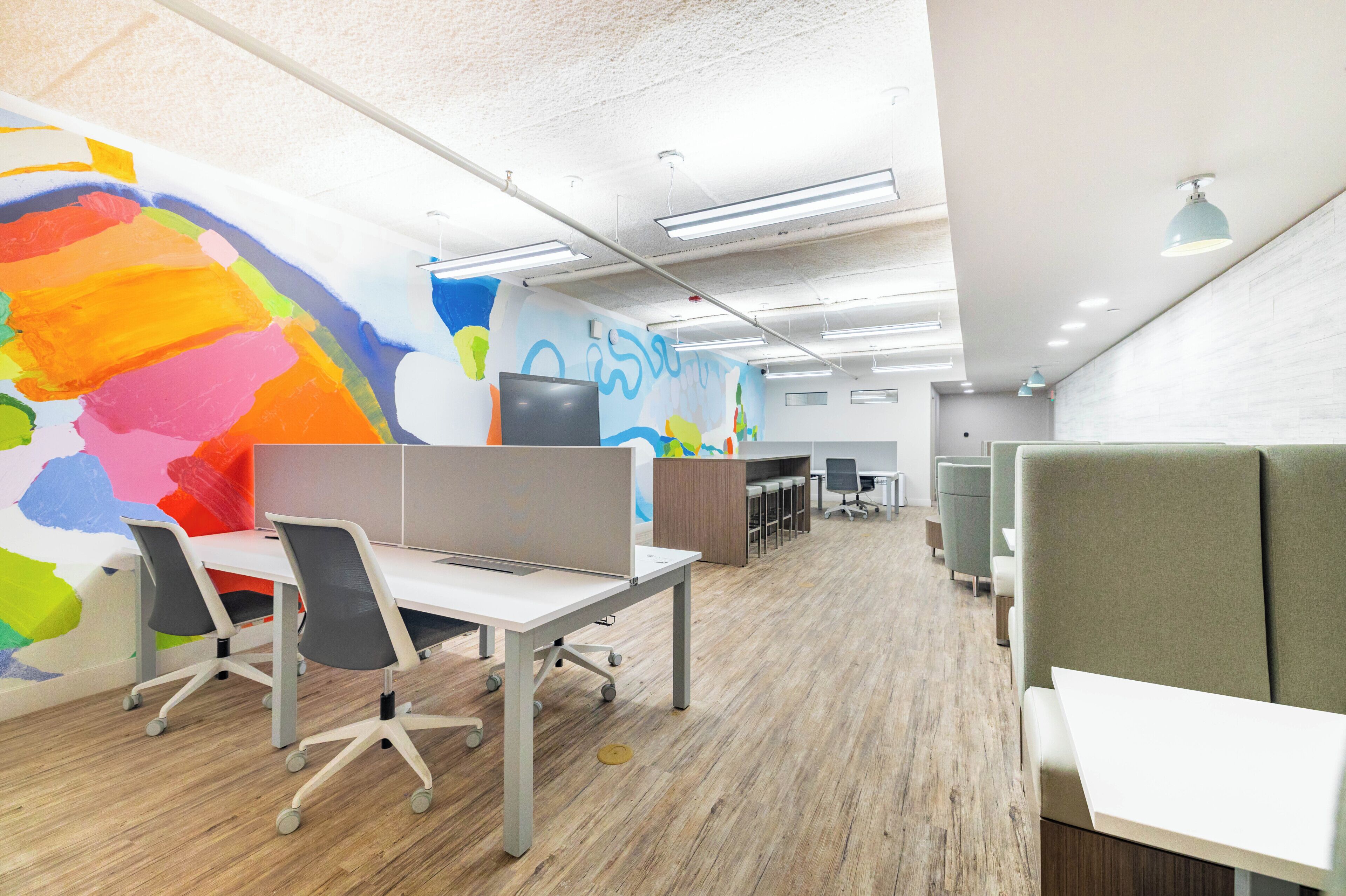 An office space with cubicles, a large colorful mural, and modern lighting.