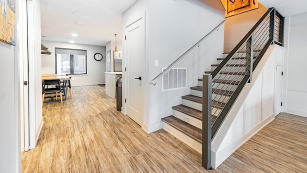 A modern interior with a wooden floor, a staircase with a metal railing, and a dining area with a table and chairs. - Stadium Suites (Ann Arbor)