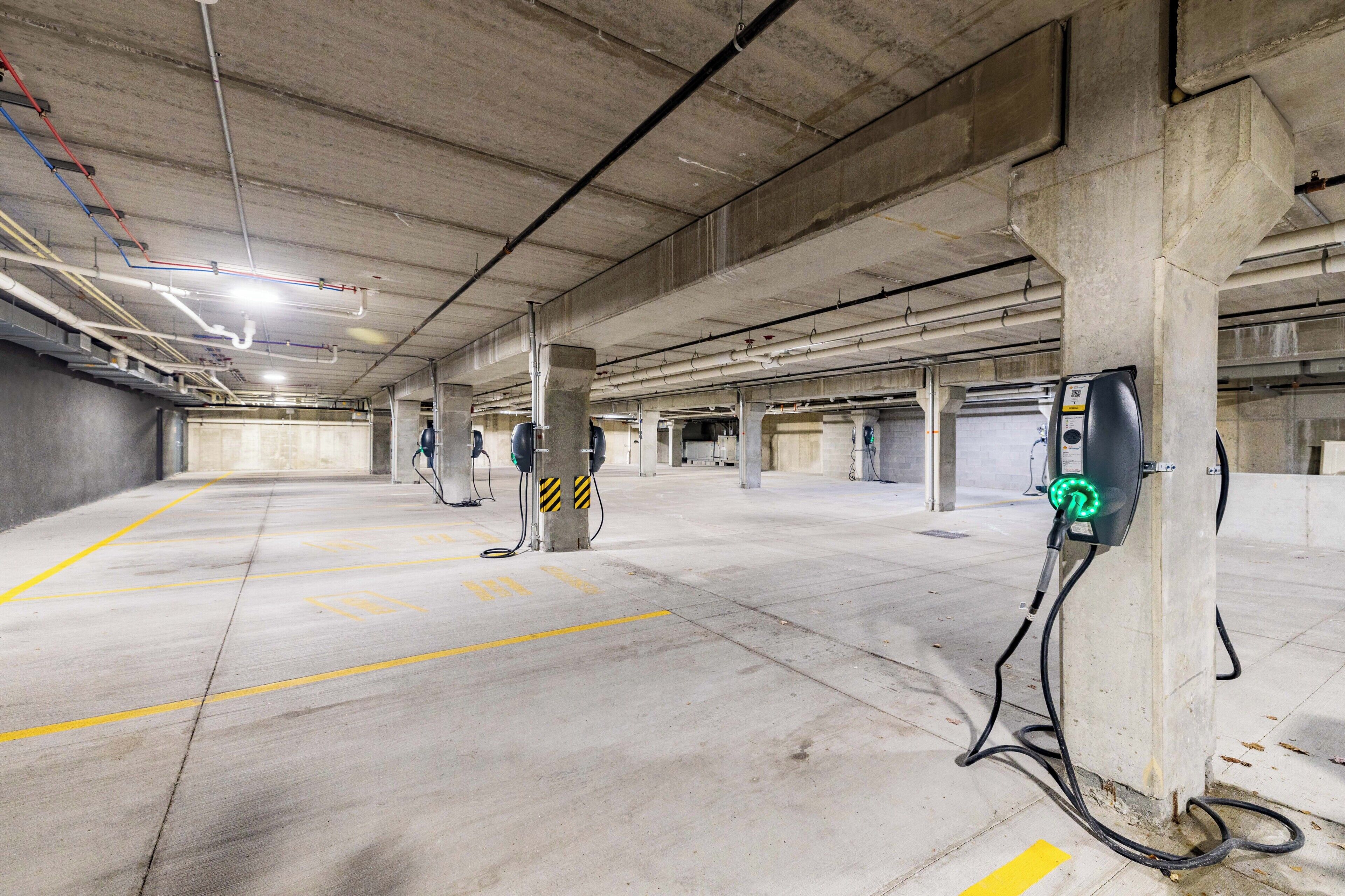 Een parkeergarage met betonnen pilaren, gele parkeerlijnen en laadpunten voor elektrische voertuigen.