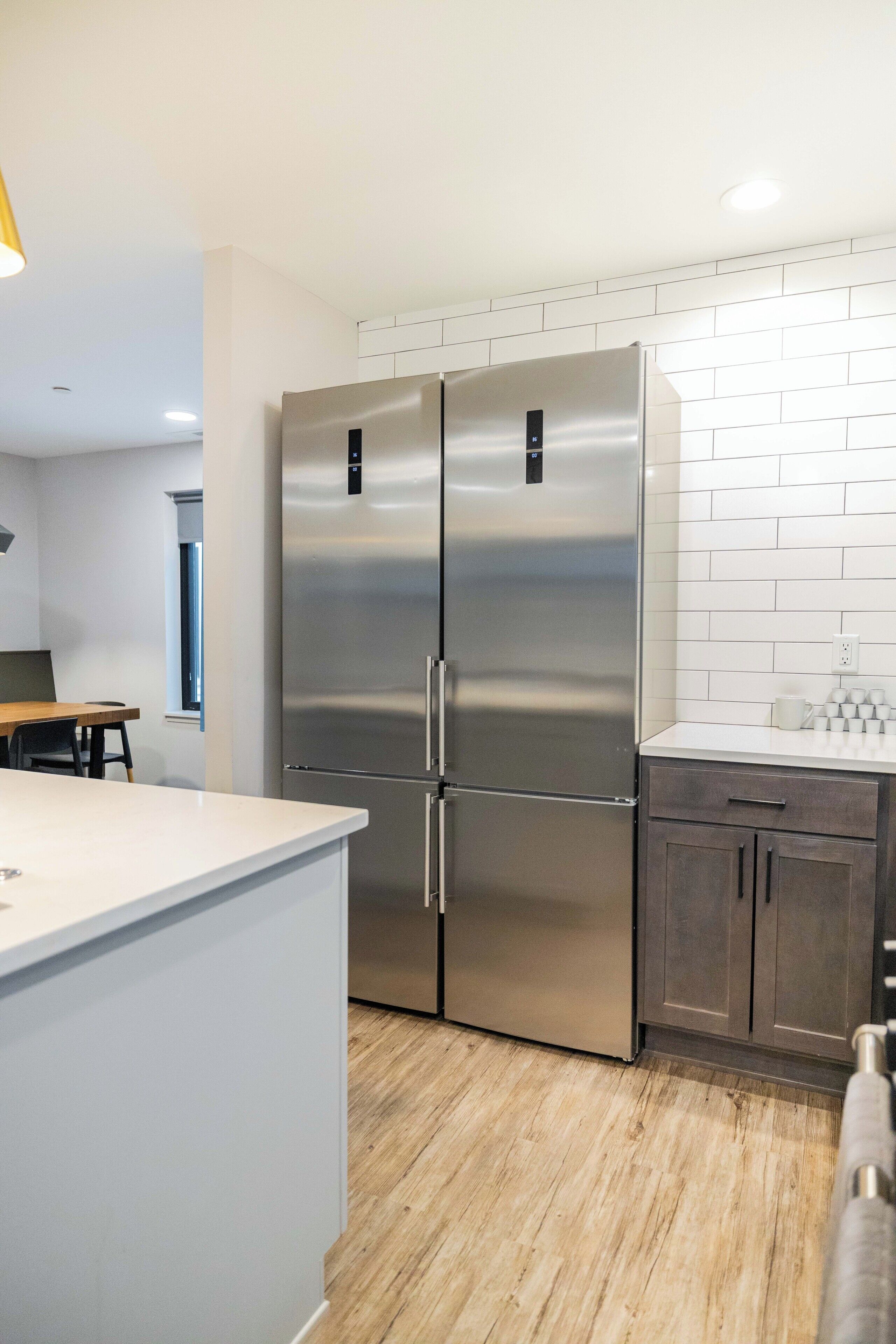 A modern kitchen with stainless steel appliances, white tiled backsplash, and wooden flooring.
