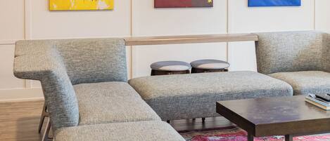 A modern living room with a gray sectional sofa, a small coffee table, and a colorful rug. There are three abstract paintings on the wall.