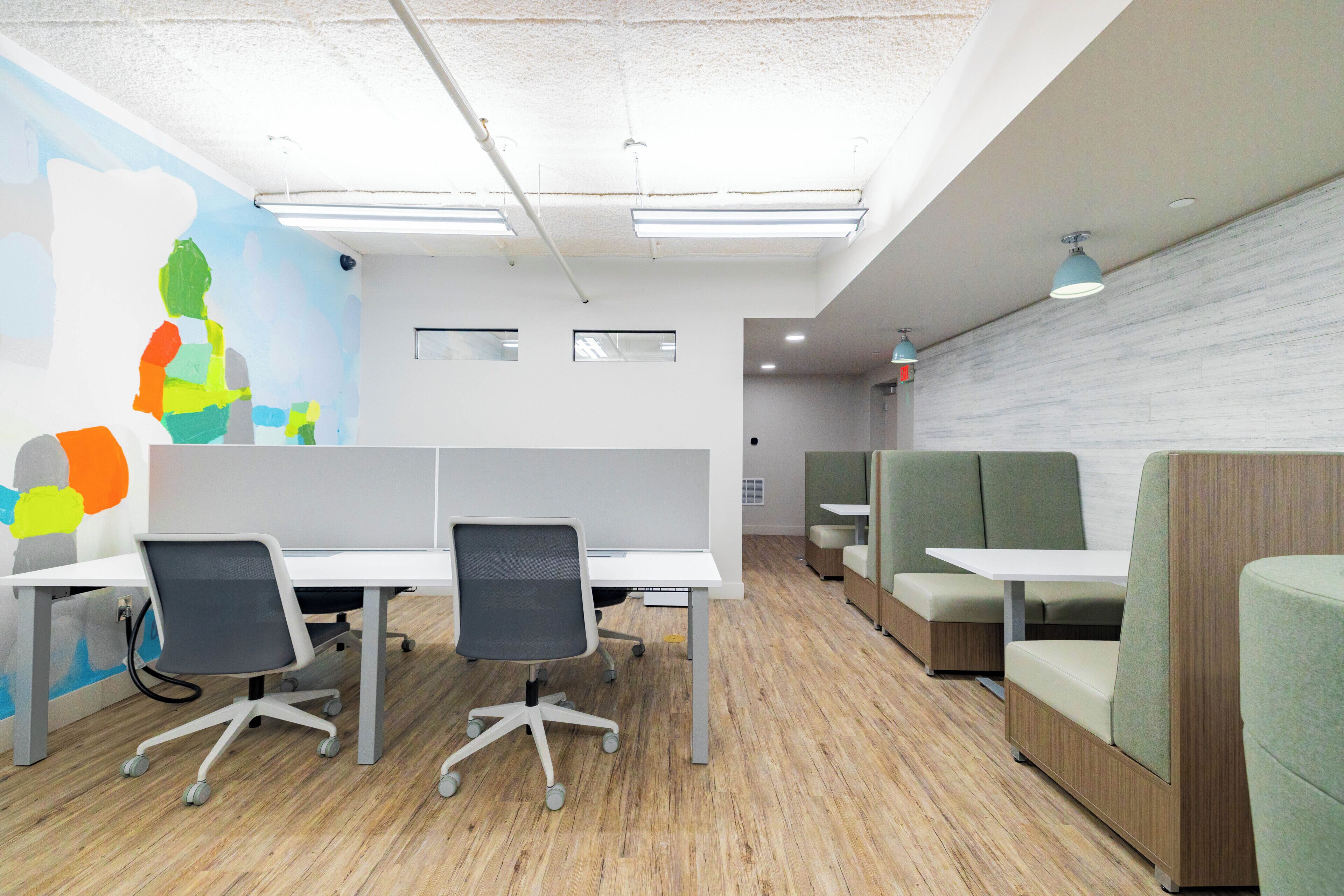 A modern office space with cubicles, a mural, and green seating areas.