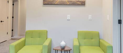 Ein Flur mit zwei grünen Sesseln, einem kleinen Tisch mit einer Lampe und einem Bild an der Wand mit der Aufschrift 'PARKING'.